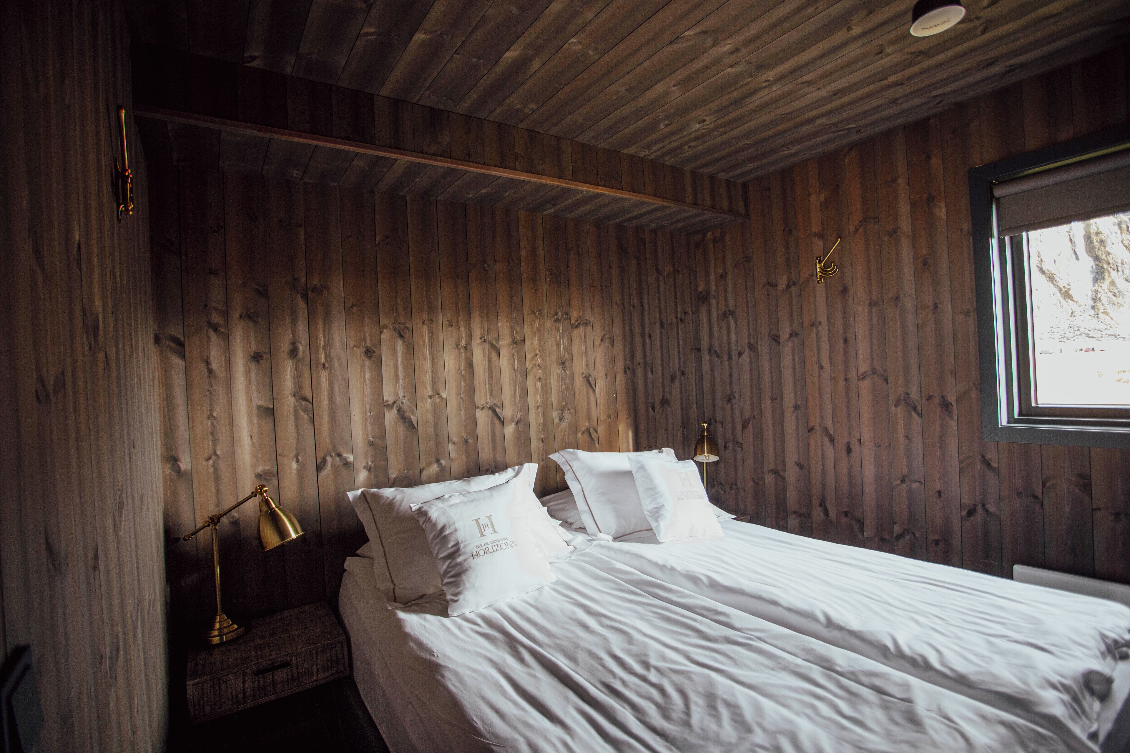 Ett sovrum med träpanel på väggarna, en säng, två sänglampor och ett fönster.