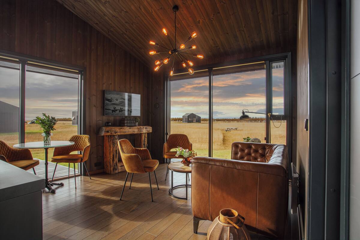 A modern interior with wooden walls, large windows, and a cozy seating area with leather chairs and a sofa.