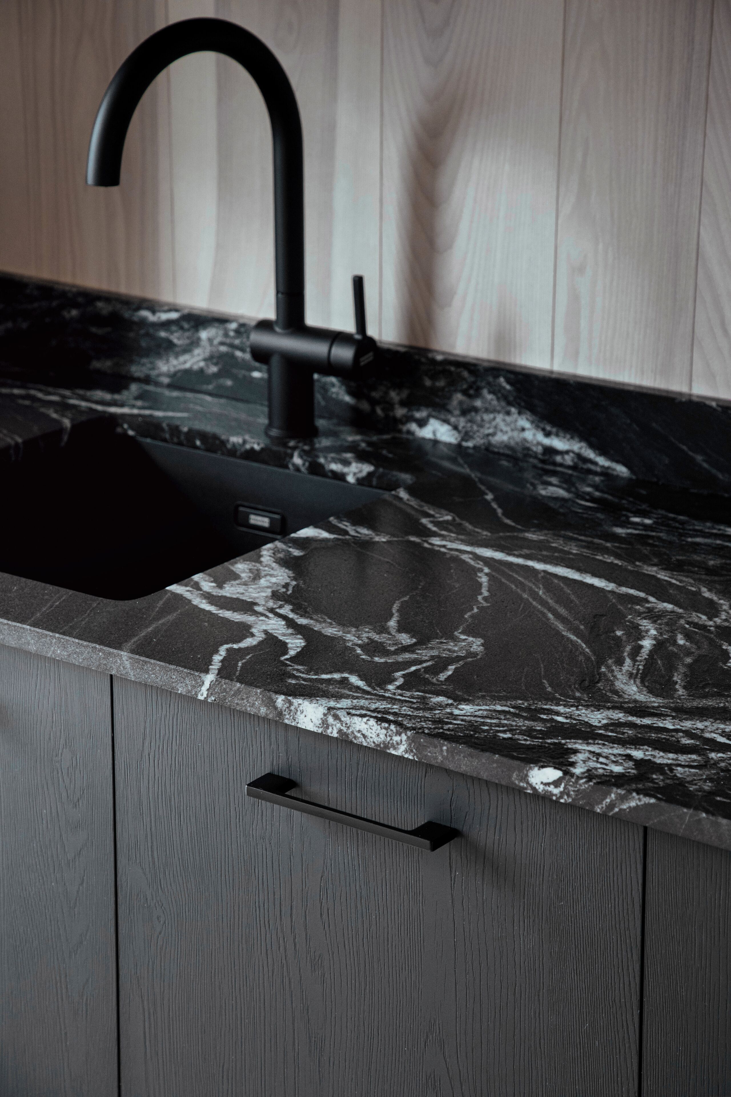 A modern kitchen with a black faucet, marble countertop, and wooden cabinets.