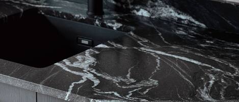 A modern kitchen with a black faucet, marble countertop, and wooden cabinets.