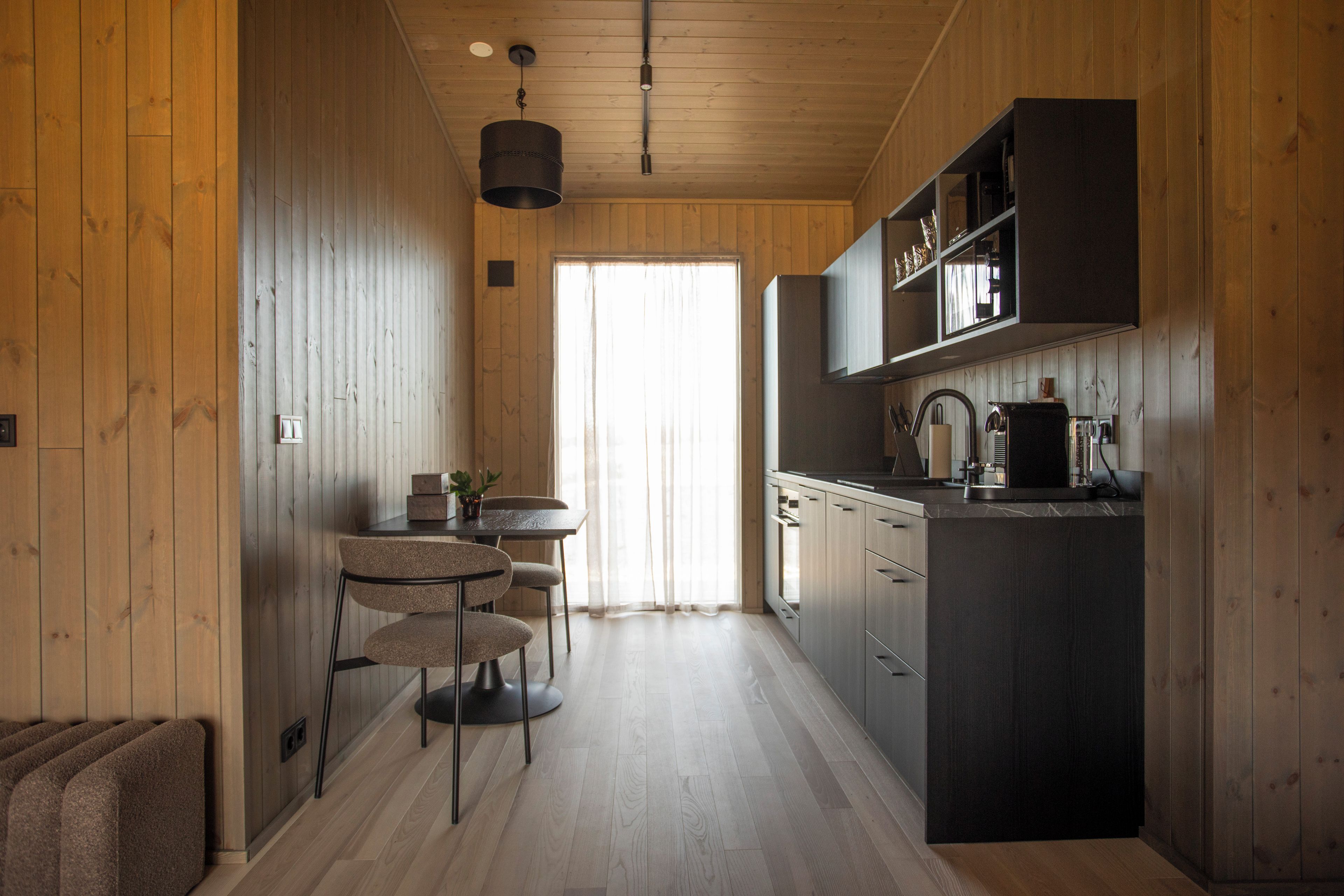 Una cocina moderna con paredes de madera, un comedor con mesa y sillas, y un ventanal grande.