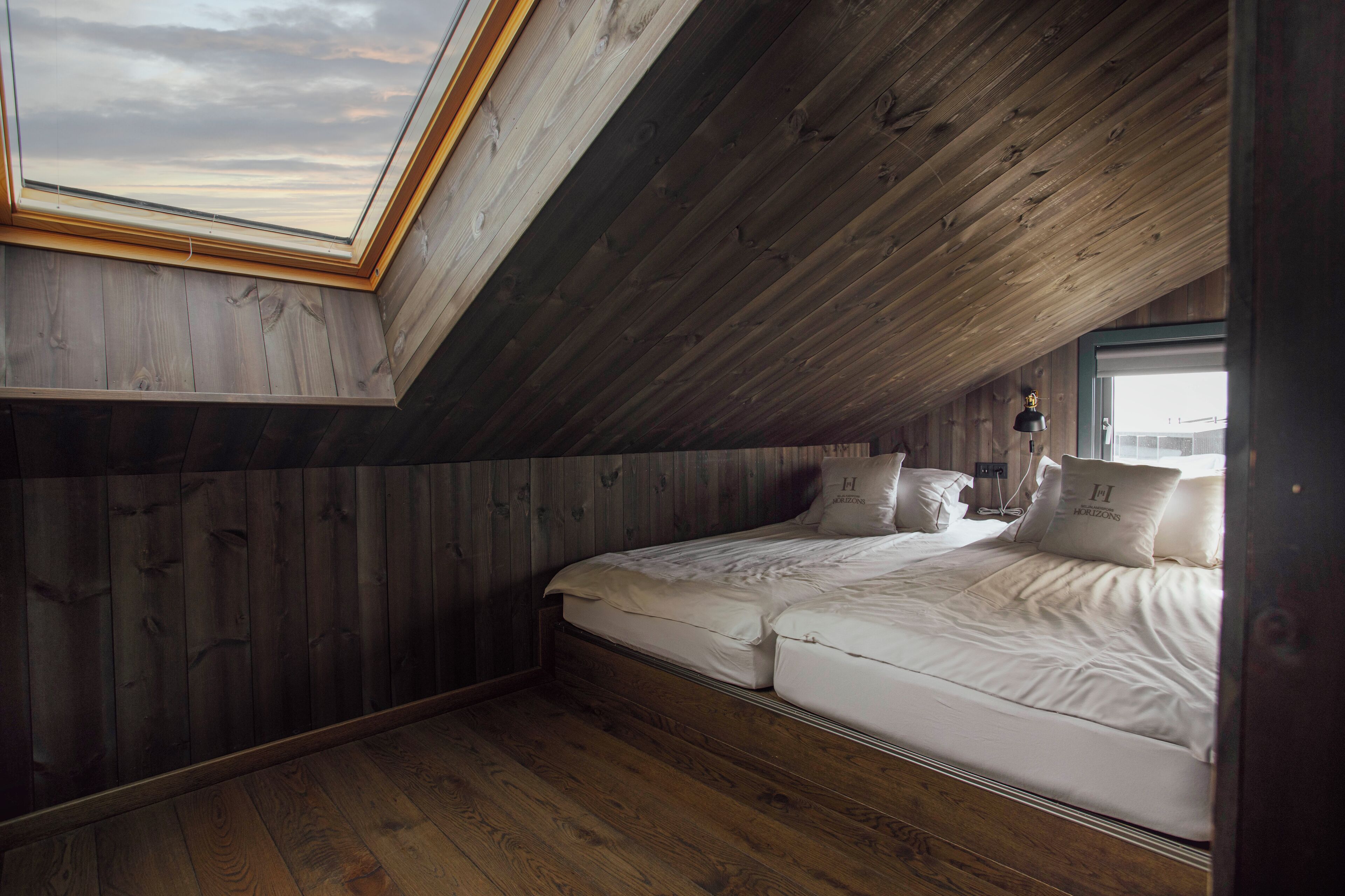 Un dormitorio con tragaluces, paredes de madera, una cama con ropa blanca y una ventana.