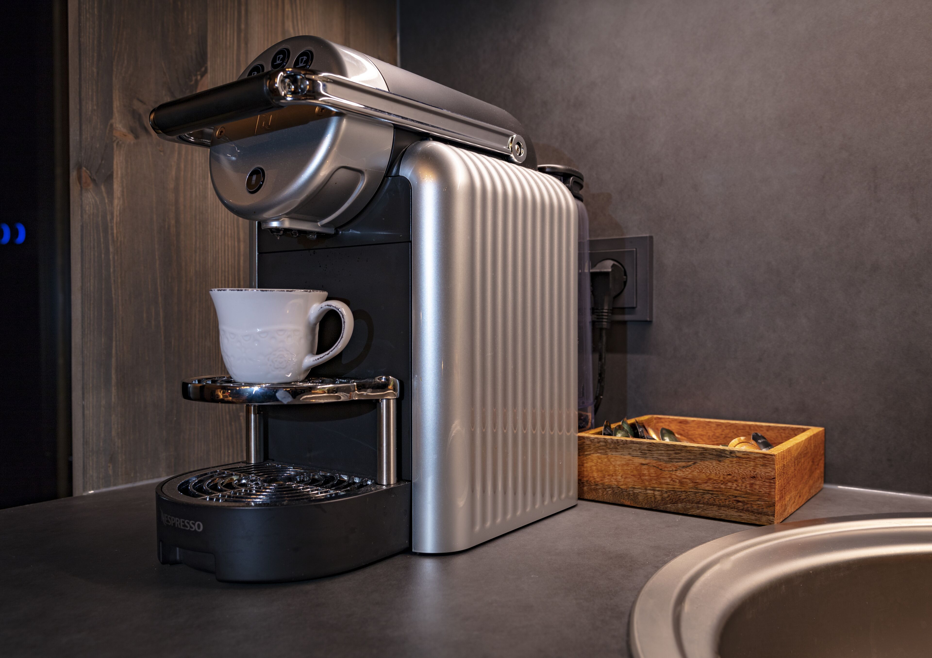 Une machine à expresso moderne dotée d’un porte-tasse, d’un moulin à café et d’une boîte en bois contenant des grains de café.