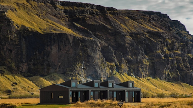 A modern building with a flat roof and large windows, surrounded by a grassy field and a steep cliff. - Seljalandsfoss Horizons (Rangárþing eystra)