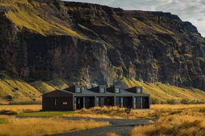 A modern building with a flat roof and large windows, surrounded by a grassy field and a steep cliff.