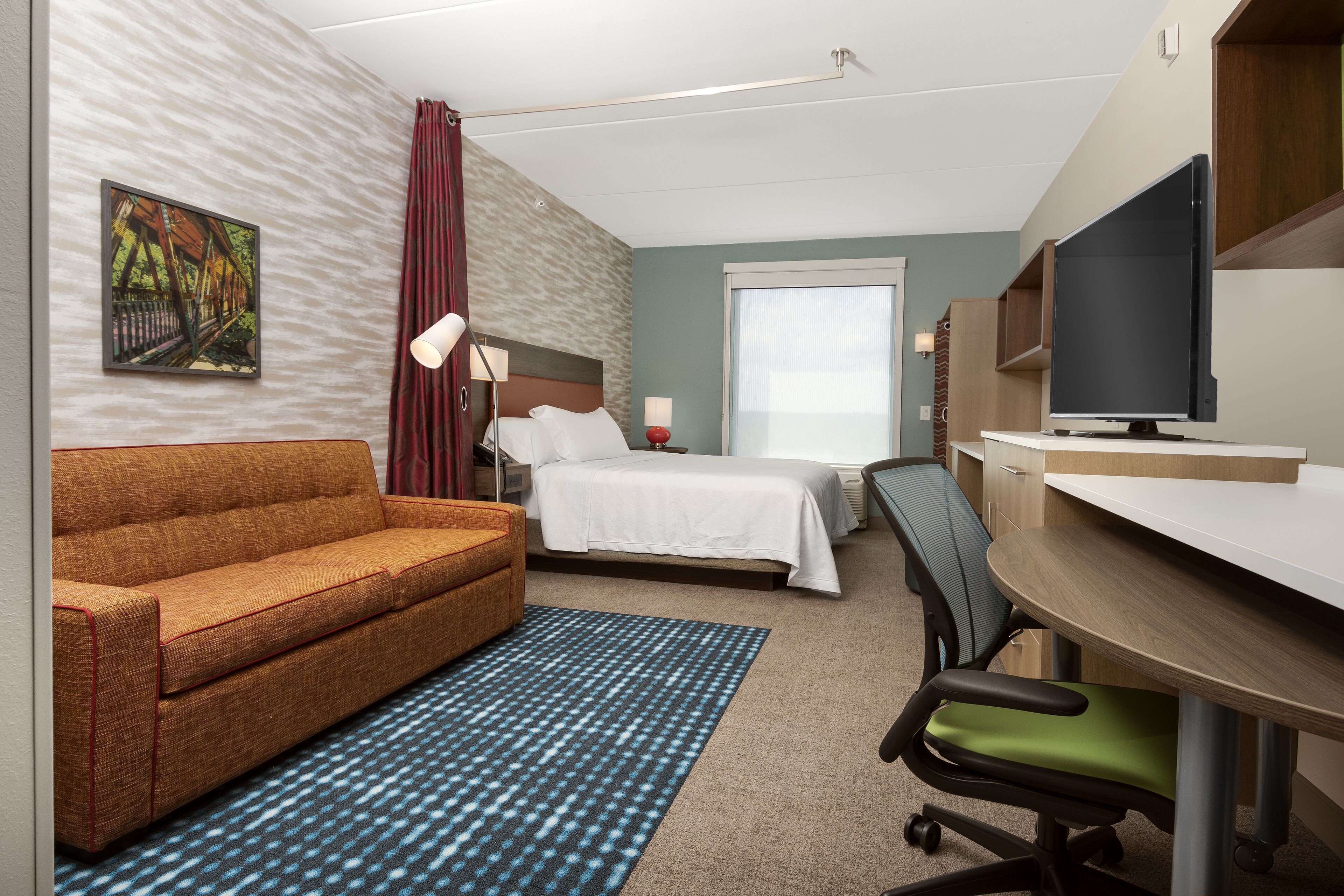 Een hotelkamer met een bed, een slaapbank, een bureau met een computer, een stoel, een televisie en een raam.