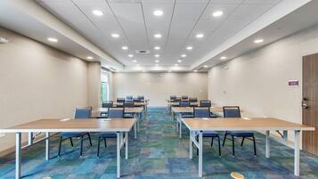 A conference room with multiple tables and chairs, carpeted floor, and ceiling lights.