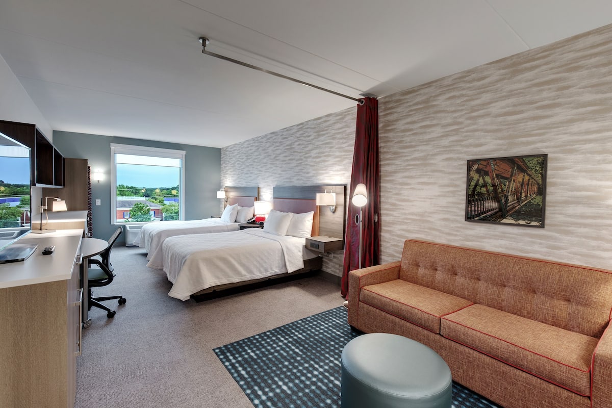 Une chambre d’hôtel équipée d’un lit, d’un bureau, d’une chaise, d’un canapé et d’une fenêtre donnant sur un paysage verdoyant.