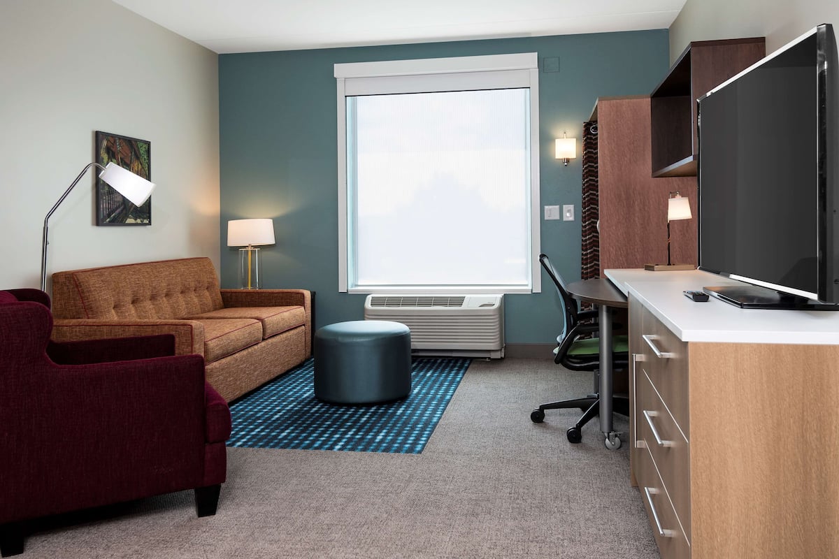 Une chambre d’hôtel compacte comprenant un canapé, un bureau, une télévision et un appareil de climatisation.