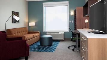 Una habitación de hotel compacta con sofá, escritorio, televisión y aire acondicionado.