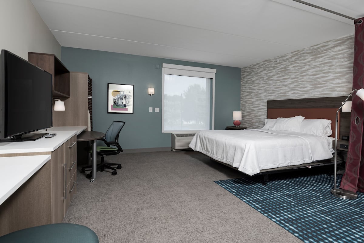 Une chambre d’hôtel équipée d’un lit, d’un bureau, d’une chaise, d’une télévision et d’une fenêtre donnant sur un paysage agréable.