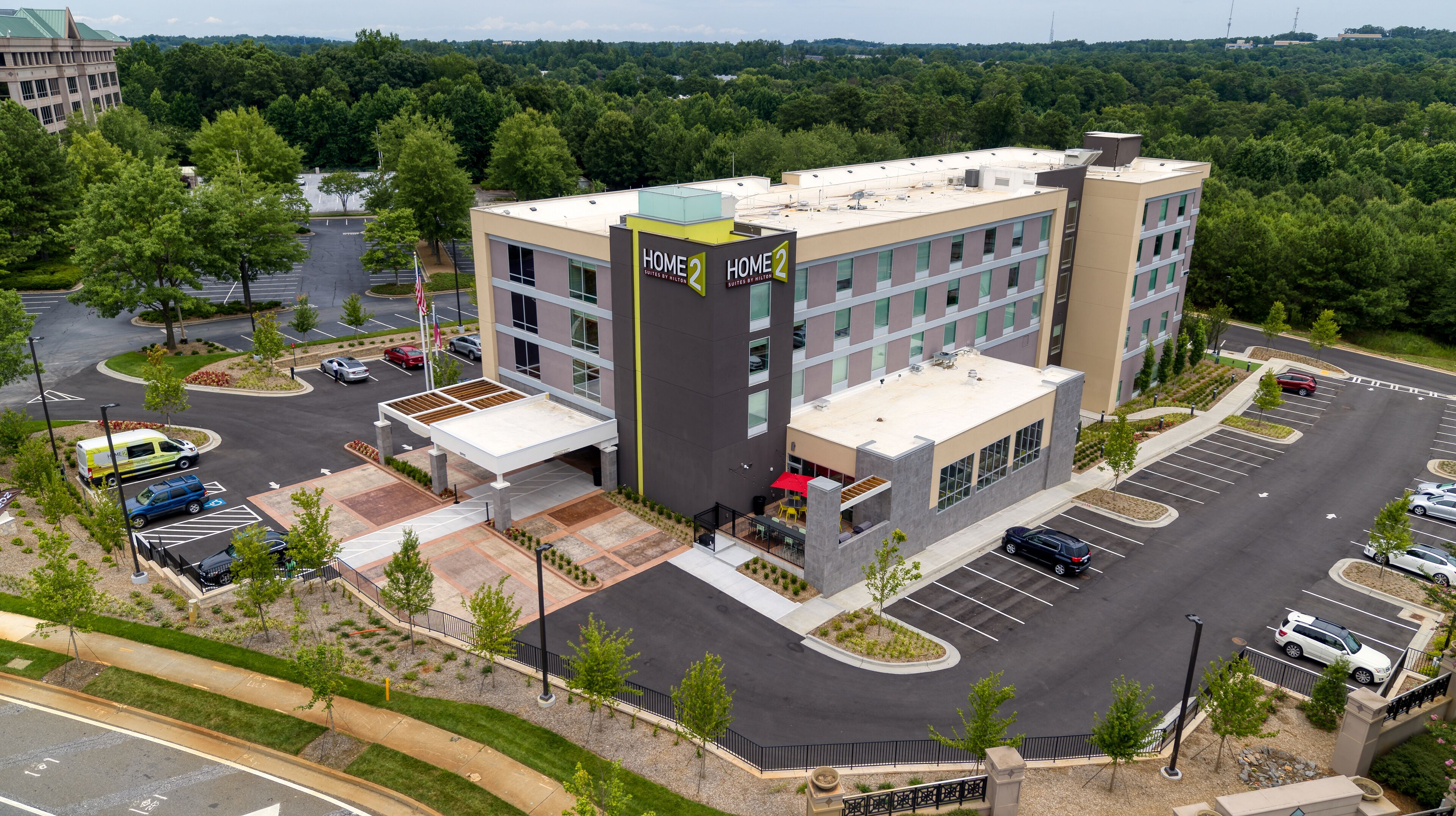A modern hotel with a central courtyard, multiple parking spaces, and a landscaped area with trees.