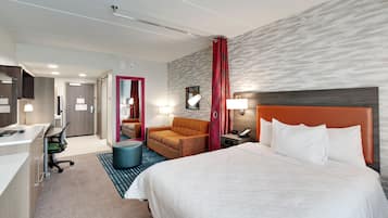 A hotel room with a bed, a desk, a chair, a sofa, and a bathroom.