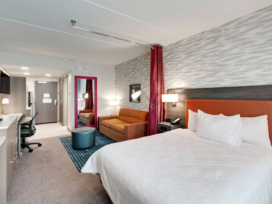 A hotel room with a bed, a desk, a chair, a sofa, and a bathroom.