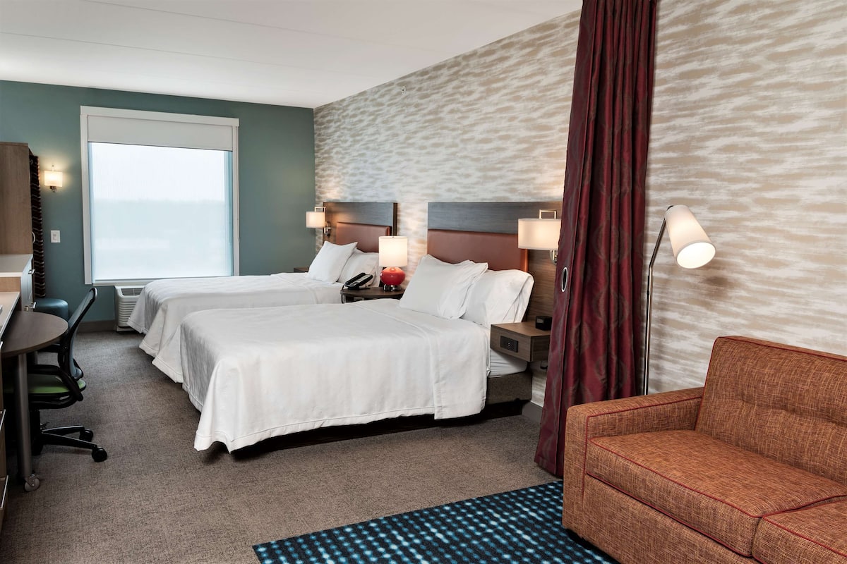 Une chambre d’hôtel avec deux lits, un bureau, une chaise et un canapé.