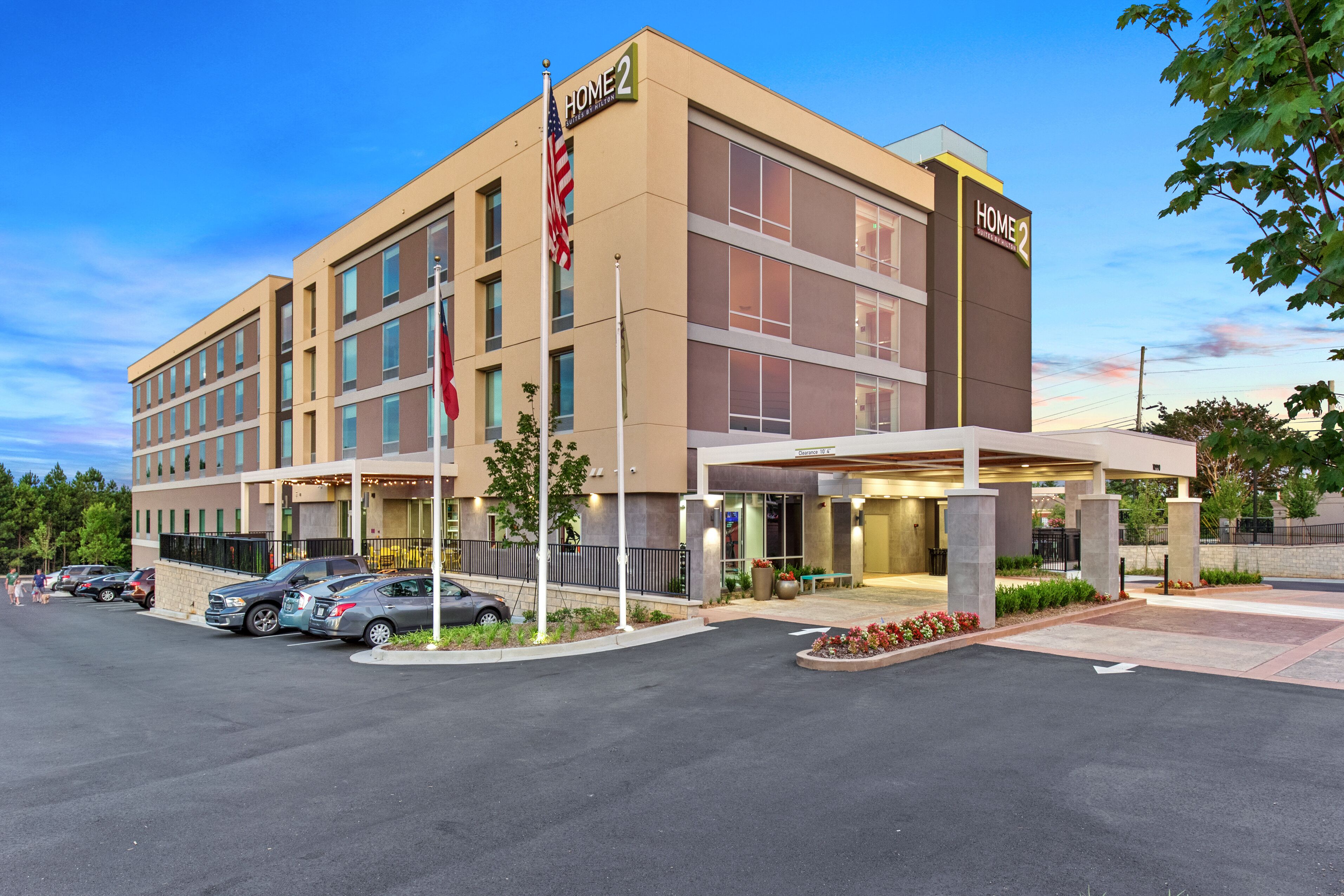 A modern hotel with a two-story structure, a covered entrance, and a parking lot with several cars.