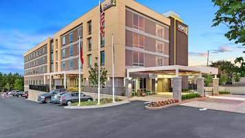 A modern hotel with a two-story structure, a covered entrance, and a parking lot with several cars.