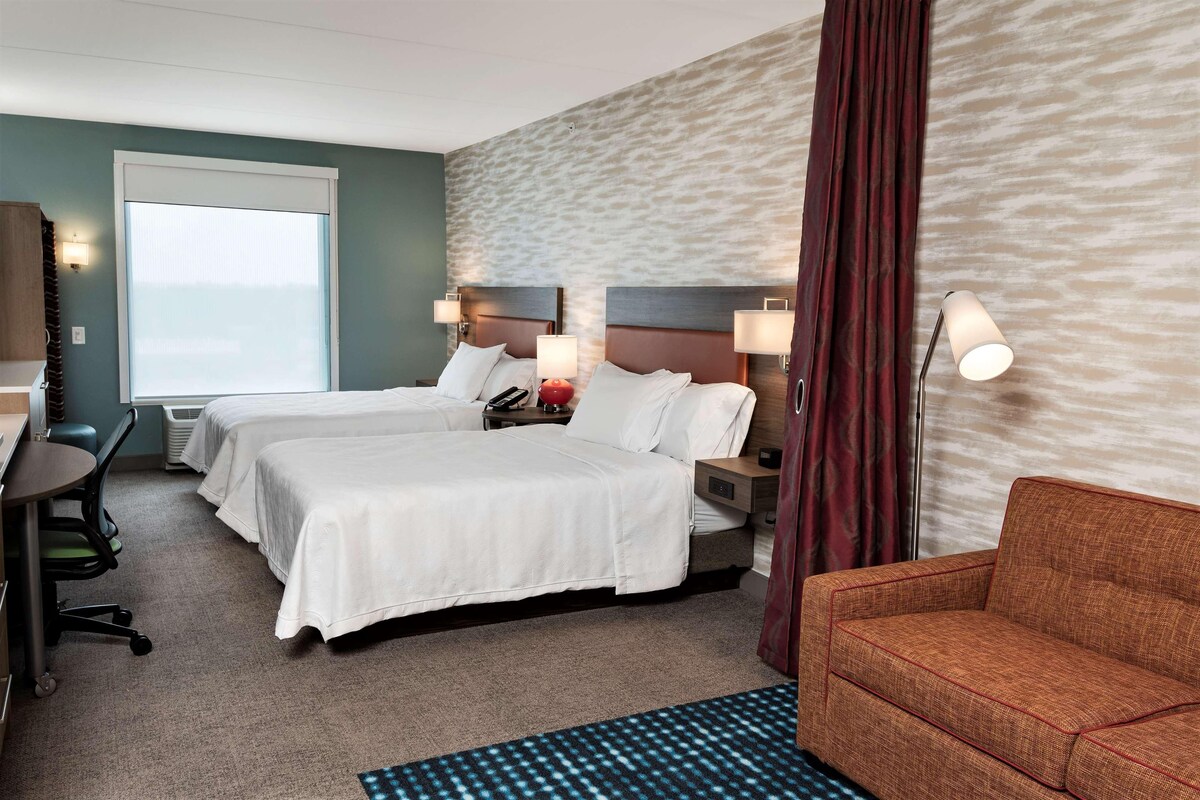 A hotel room with two beds, a desk, a chair, and a sofa.