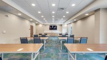 A conference room with multiple tables and chairs, a carpeted floor, and a flat-screen TV on the wall.