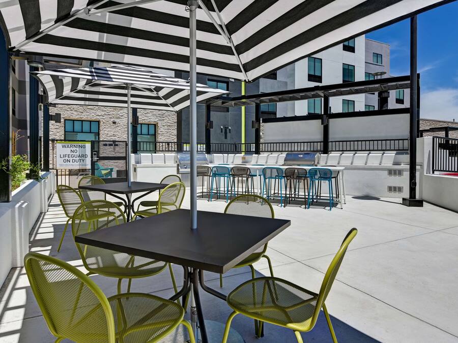 An outdoor seating area with tables and chairs, a lifeguard sign, and a view of a modern building.