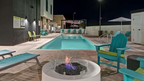 A poolside area with lounge chairs, a fire pit, and a bar area.