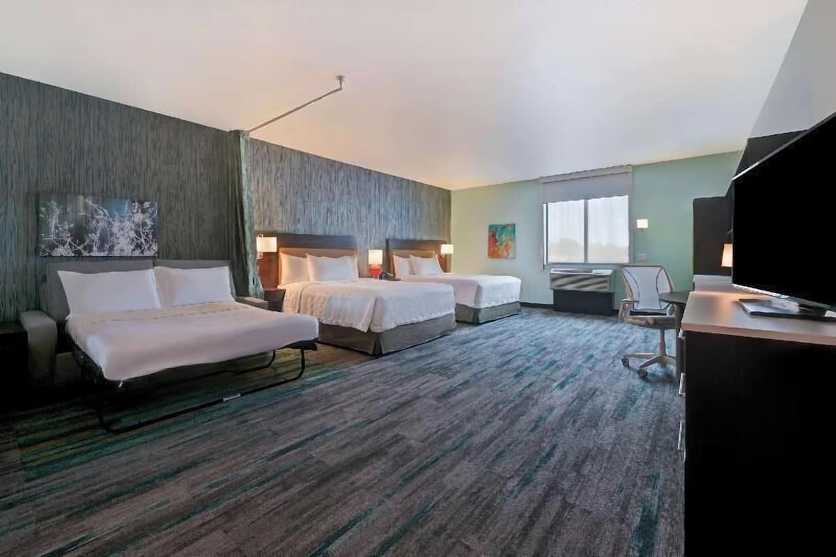 Een hotelkamer met twee bedden, een bureau, een stoel, een televisie en een raam.