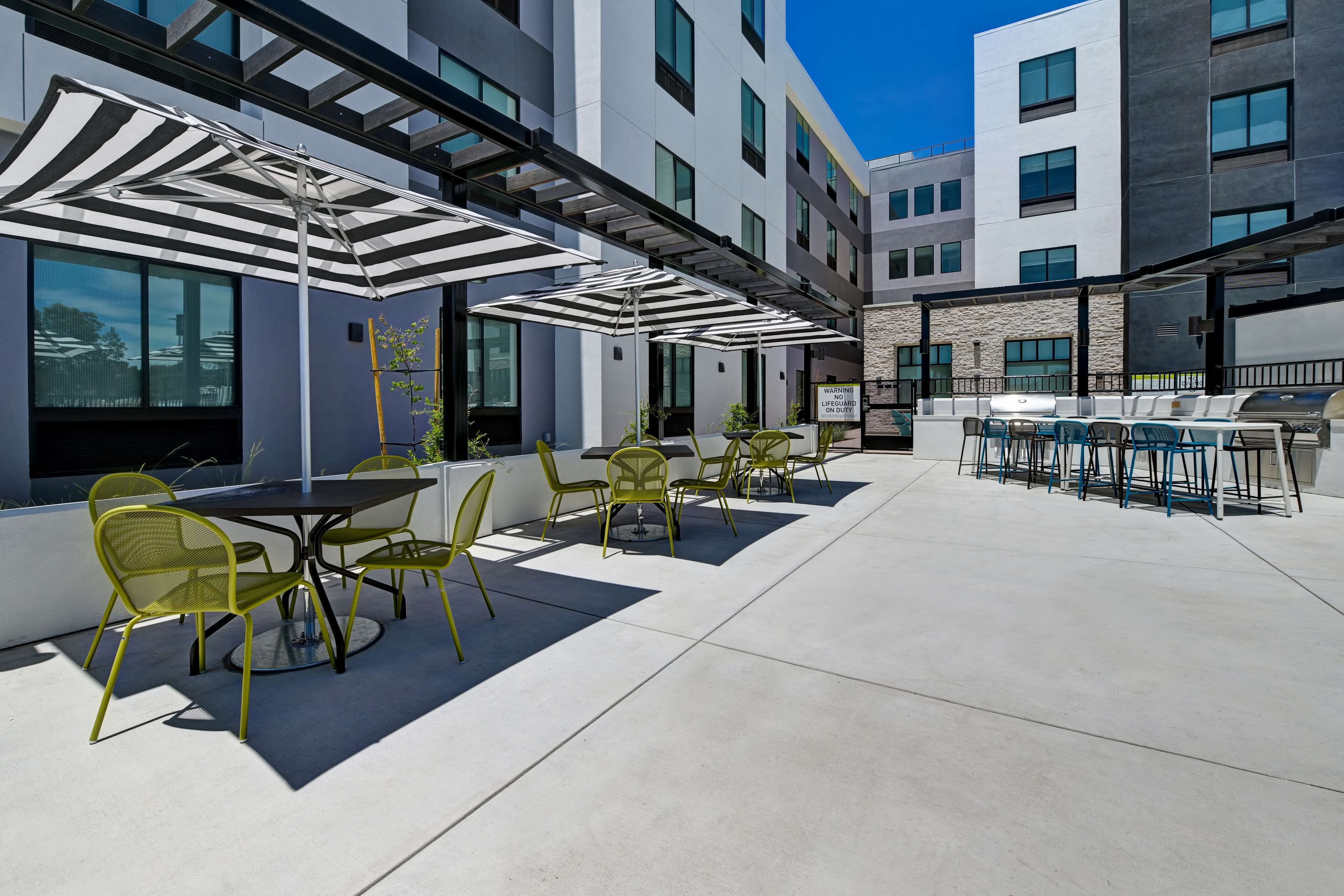 An outdoor patio with tables and chairs, a grill, and umbrellas.