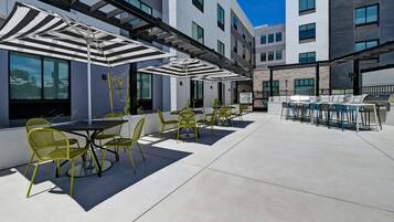 An outdoor patio with tables and chairs, a grill, and umbrellas.