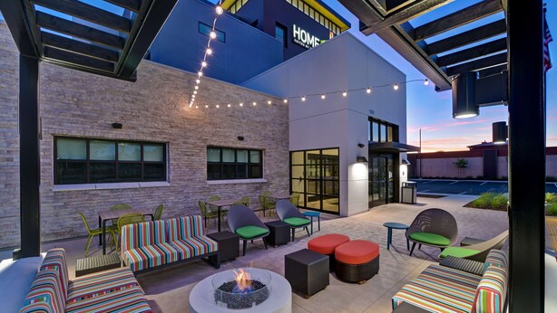 A modern outdoor seating area with a fire pit, colorful striped sofas, and green chairs.
