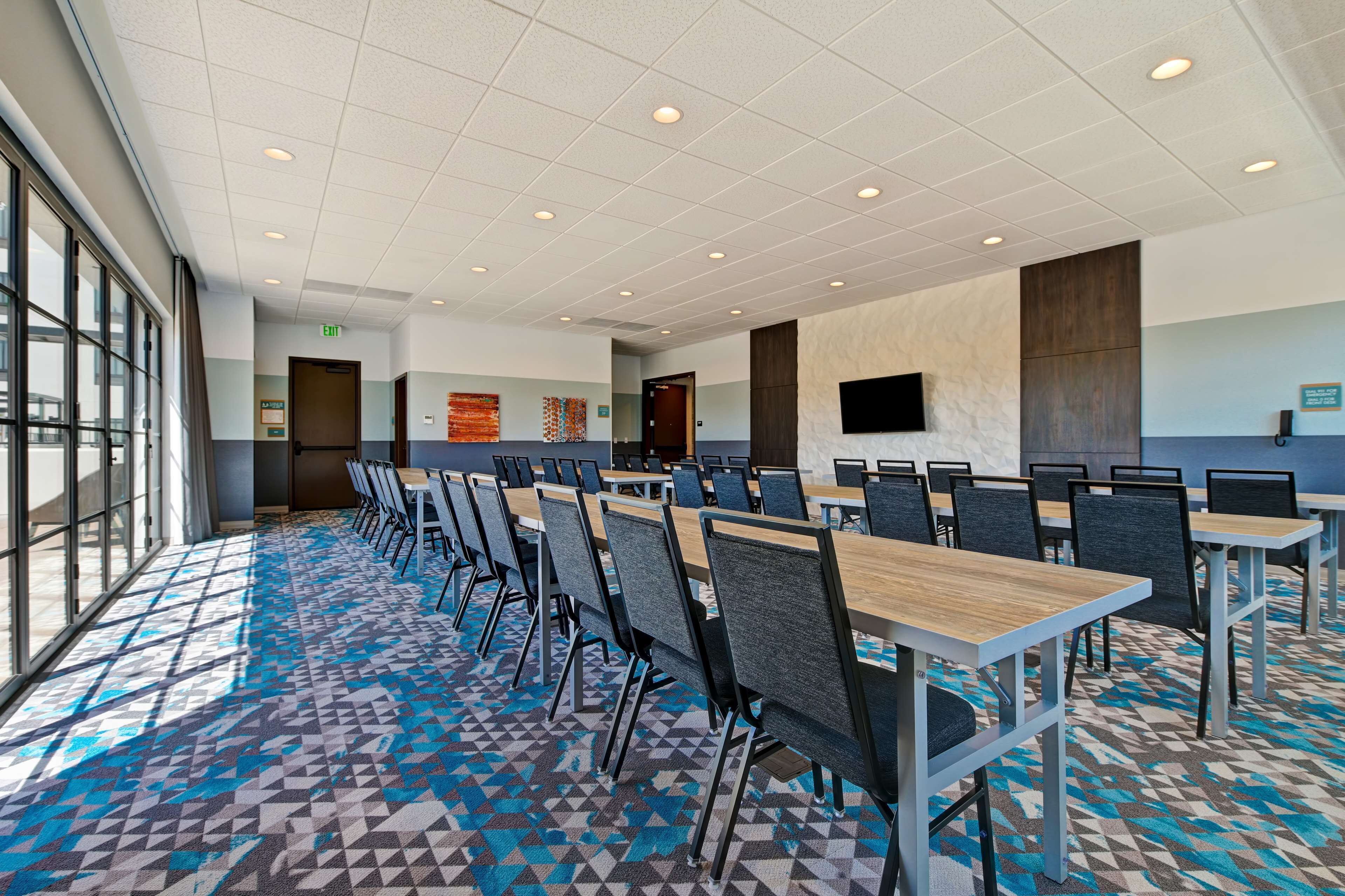 A conference room with long tables and chairs, a patterned carpet, and a large window on one side.