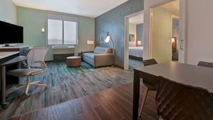 A hotel room with a desk, chair, sofa, and a dining table.