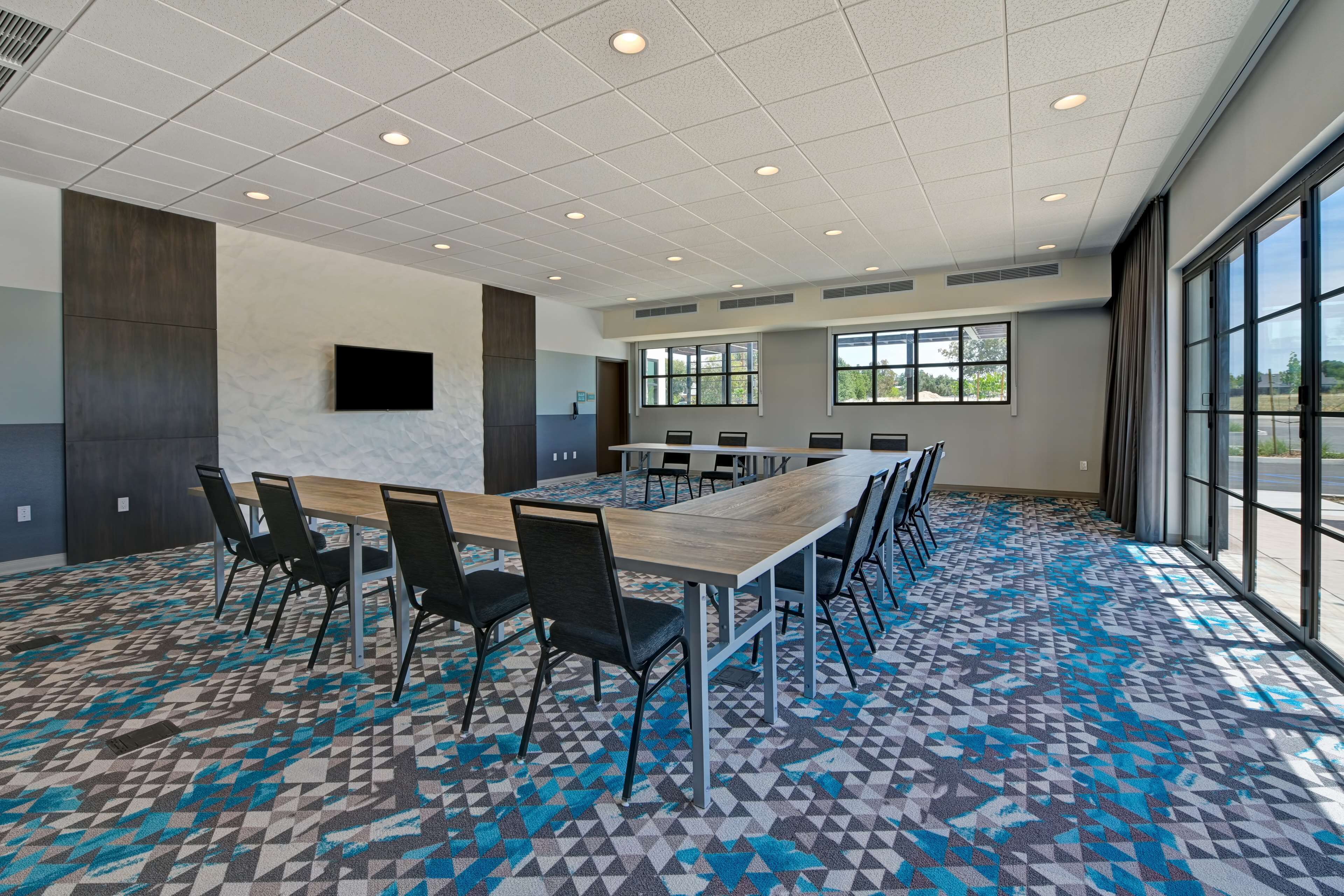 Un salón de conferencias con una larga mesa, sillas, un televisor de pantalla plana y ventanas grandes.
