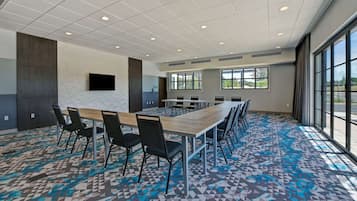 Un salón de conferencias con una larga mesa, sillas, un televisor de pantalla plana y ventanas grandes.