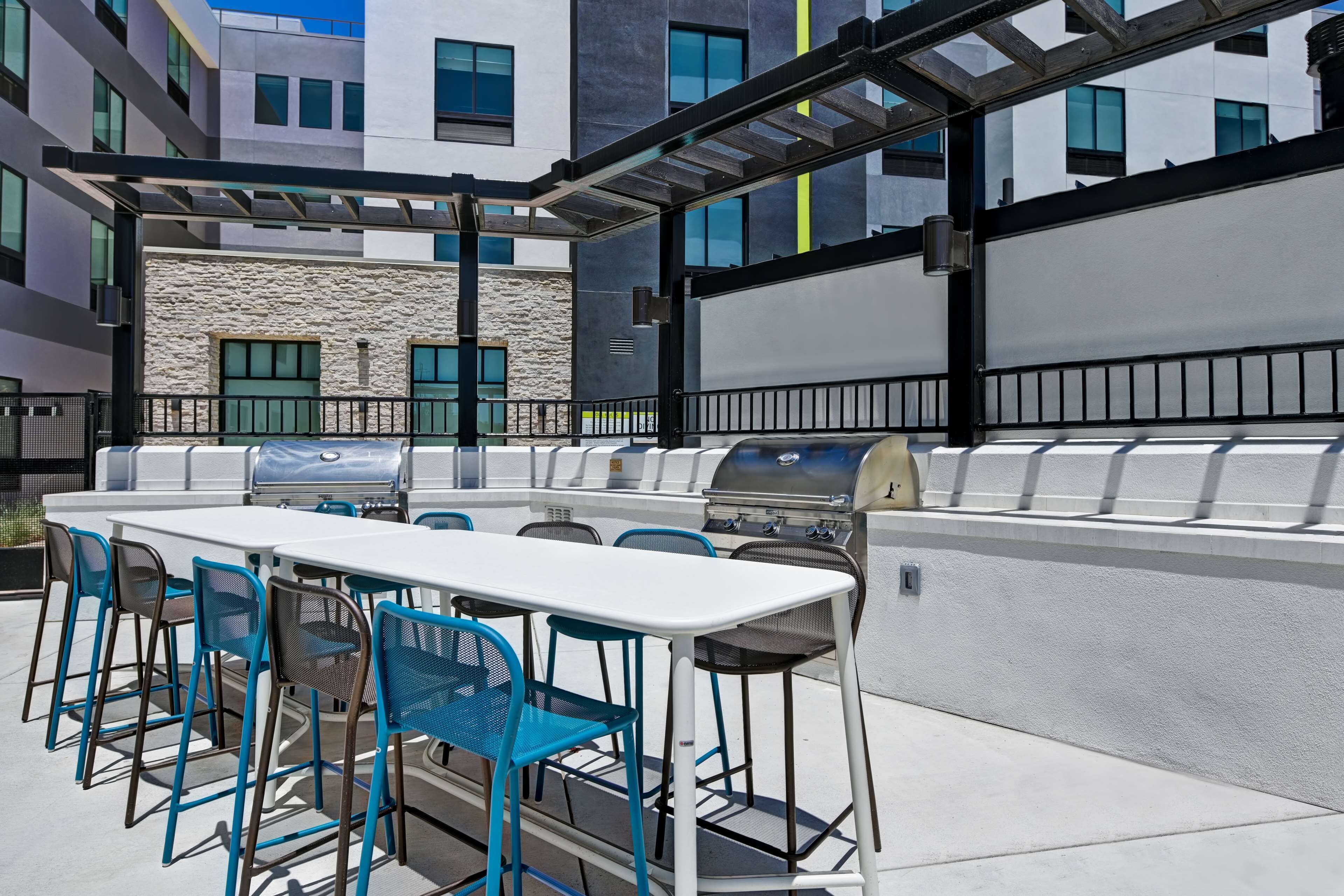 An outdoor patio with a white table and blue chairs, a grill, and a stone wall.