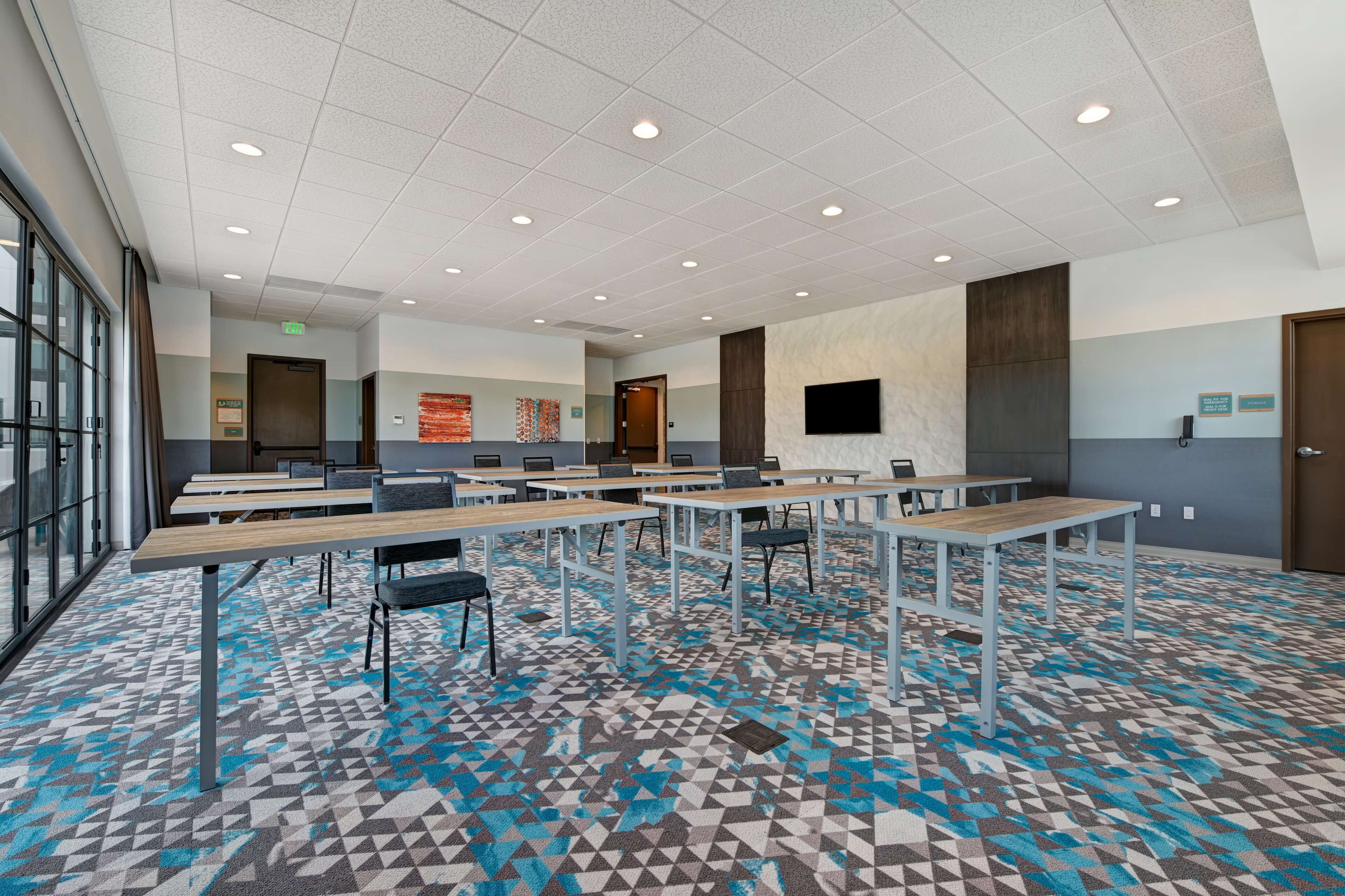 A conference room with tables and chairs, a patterned carpet, and a large window on one side.