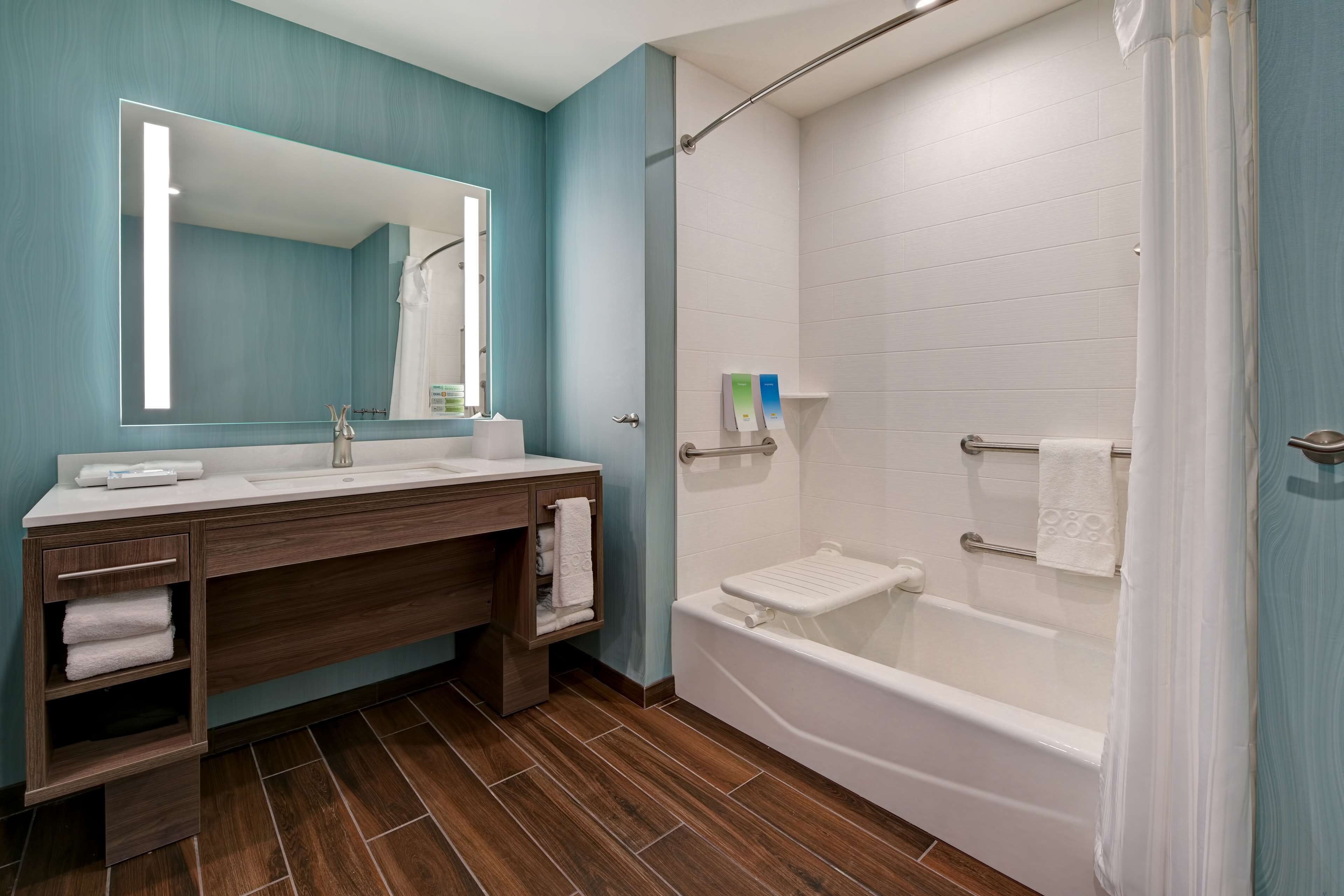 Un bagno moderno con uno specchio grande, un mobile bagno in legno, una vasca e uno spazio doccia.