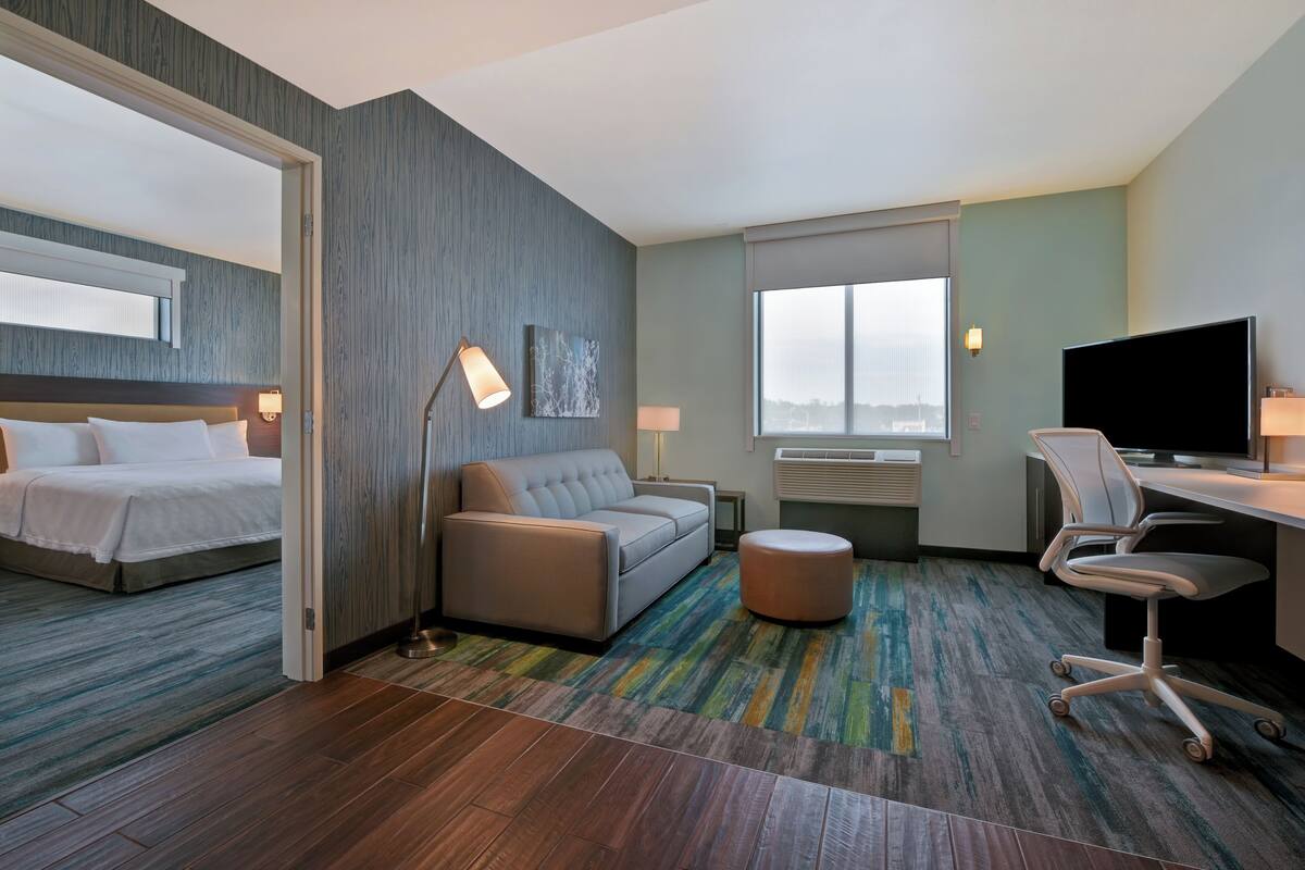 Een hotelkamer met een bed, een slaapbank, een bureau met stoel, een televisie en een groot raam.