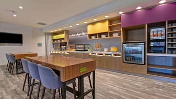 A modern kitchen area with a wooden bar, seating, a refrigerator, and shelves with kitchenware.