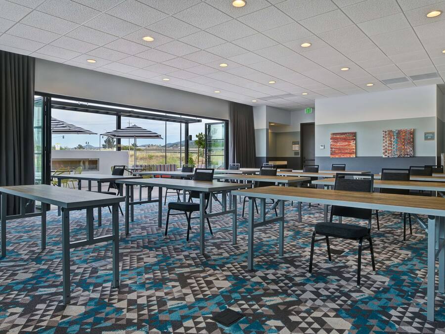 A conference room with tables and chairs, large windows, and a patterned carpet.