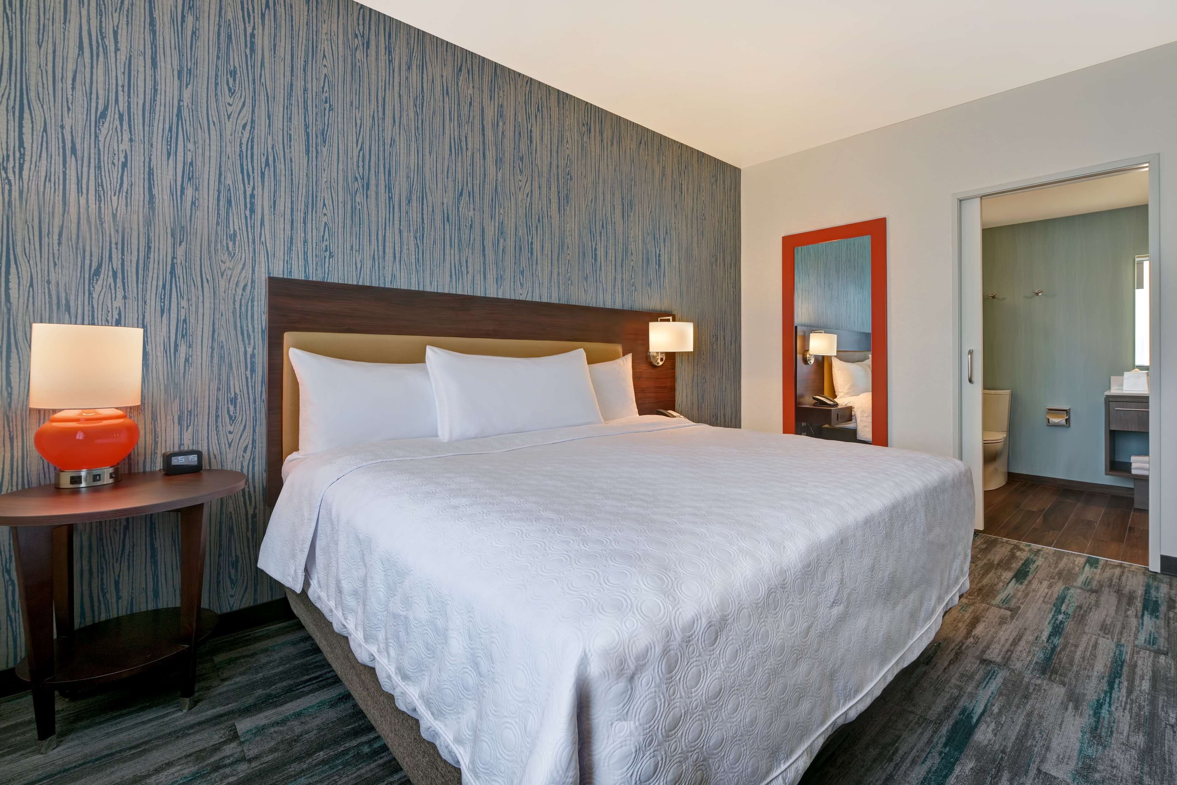 Ein Hotelzimmer mit einem großen Bett, zwei Nachttischlampen, einem Nachttisch und einem Spiegel.