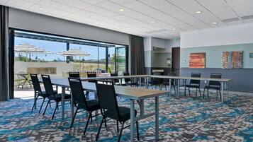 A modern conference room with large tables and chairs, a patterned carpet, and large windows offering a view of the outdoors.