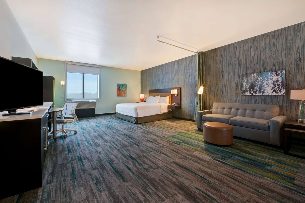 Een hotelkamer met een bed, een sofa, een bureau met een televisie en een groot raam.