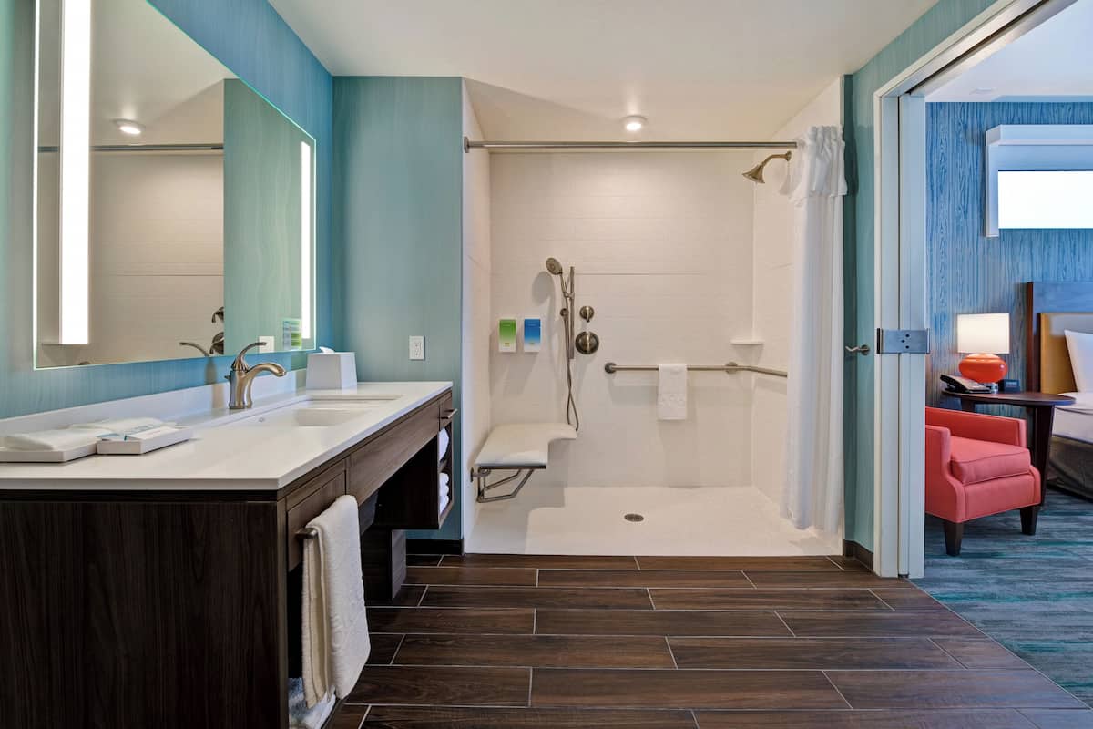 Een moderne badkamer met een grote spiegel, twee wasbakken, een douchegedeelte en een rode stoel.
