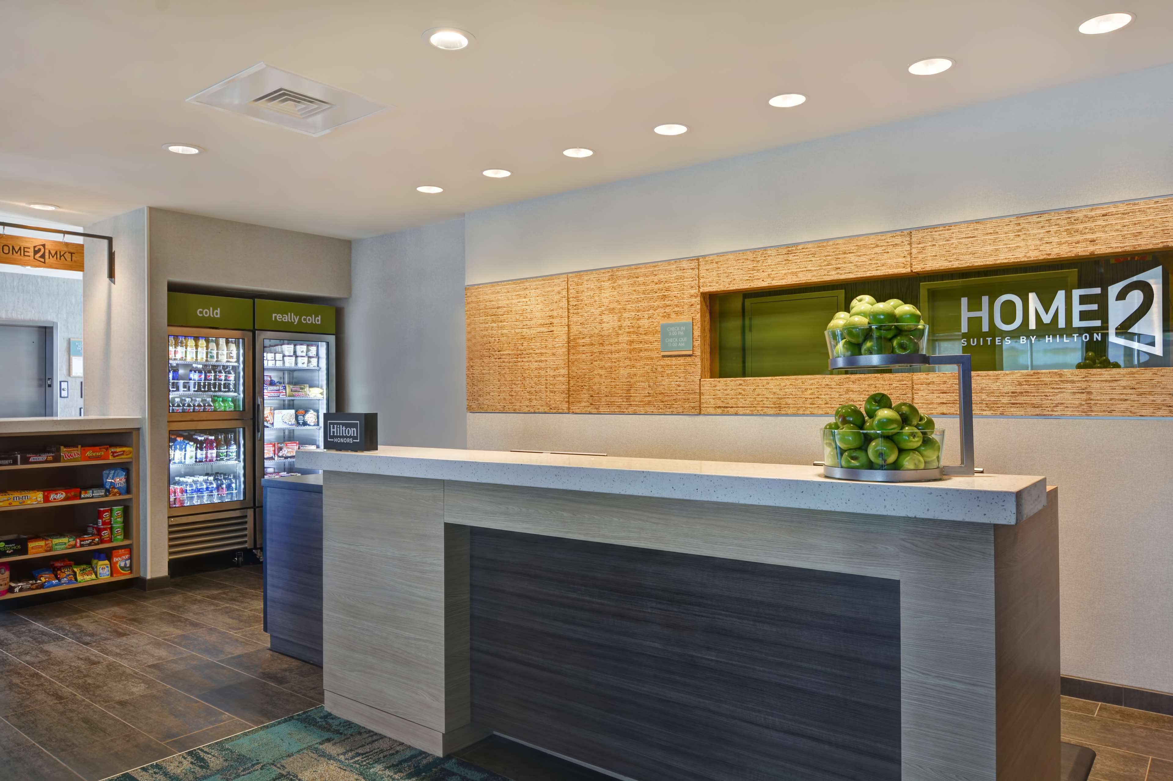 A hotel reception area with a modern design, including a reception desk, a minibar, and a refrigerator stocked with beverages.