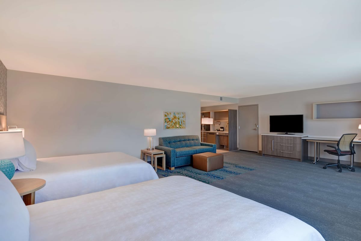 Ein Hotelzimmer mit zwei Betten, einem Schlafsofa, einem Schreibtisch, einem Fernseher und einer Küchenzeile.