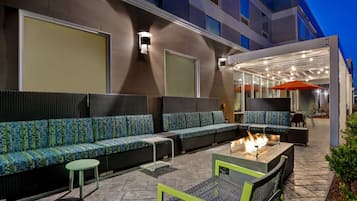 An outdoor seating area with a fire pit, cushioned seating, and a covered section with tables and chairs.