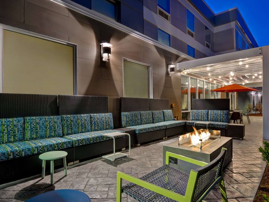 An outdoor seating area with a fire pit, cushioned seating, and a covered section with tables and chairs.