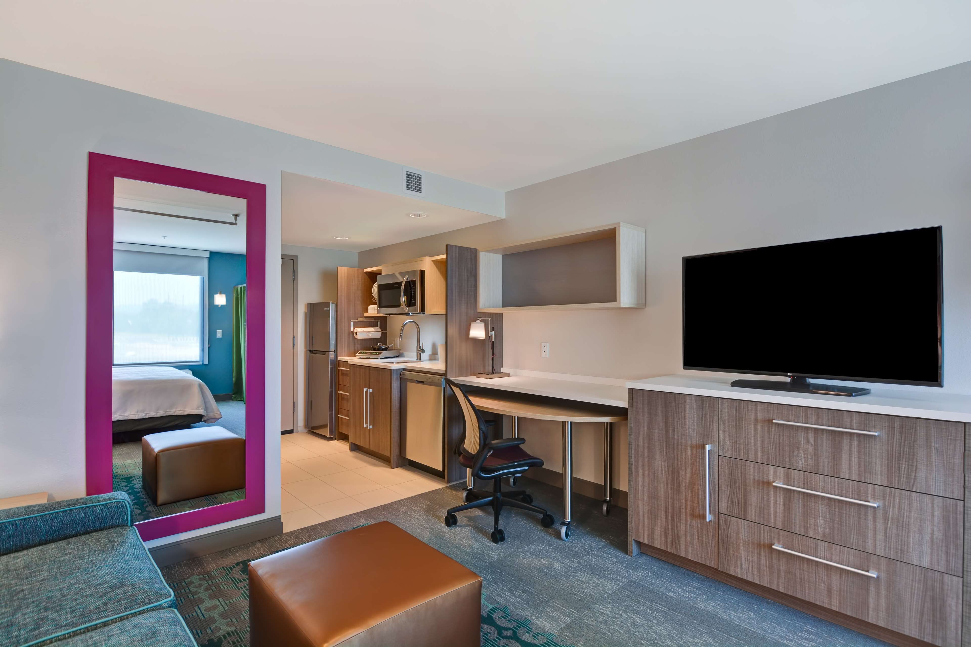 Habitación de hotel con cama, escritorio, televisión y baño visible a través de una puerta abierta.