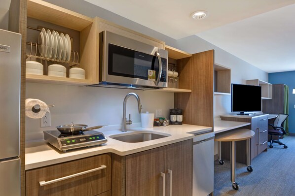 Una cocina moderna con microondas, estufa, pileta y un pequeño comedor con televisor y escritorio.