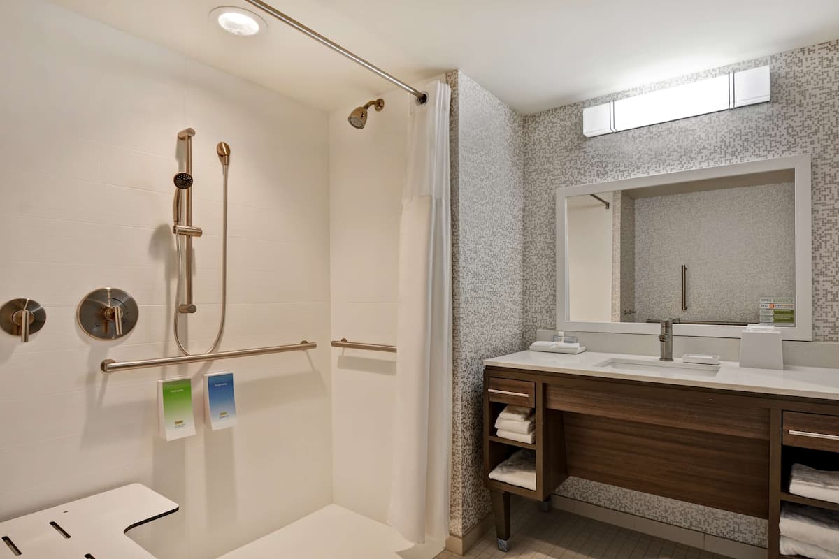 Ein modernes Badezimmer mit barrierefreier Dusche, einem Waschtisch mit Spiegel und einer Toilette.